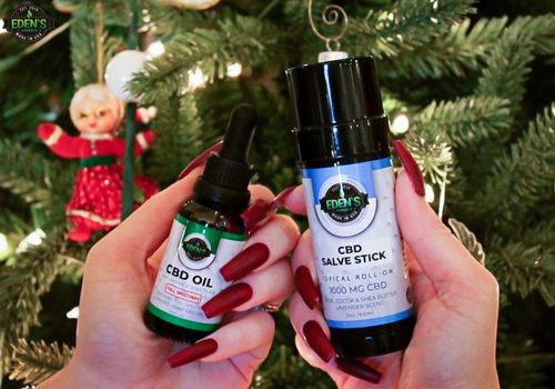 woman holding eden's herbals cbd salve and oil infront of a christmas tree