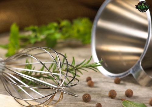 kitchen whisk and bowl next to herbs on a counter top