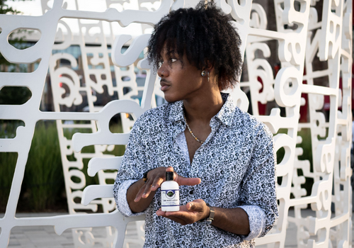 Smiling young man holding up a bottle of cbd body lotion from edens herbals