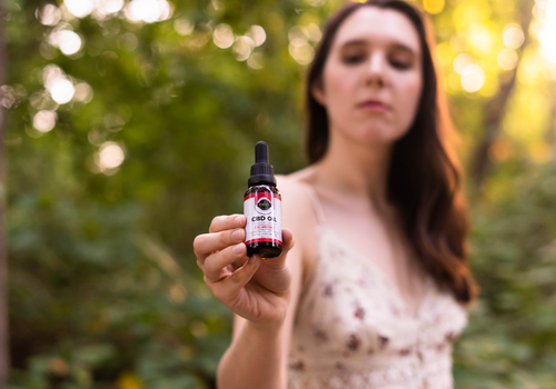 Woman in sunny forest holding up tincture of cinnamon flavored full spectrum cbd oil
