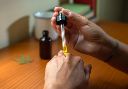 Closeup of hands holding a cbd oil tincture and applying some to the back of one hand