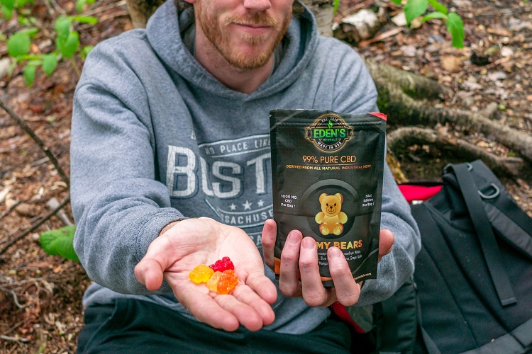 Hand extended outward offering assorted fruit flavored CBD gummy bears from Eden's Herbals