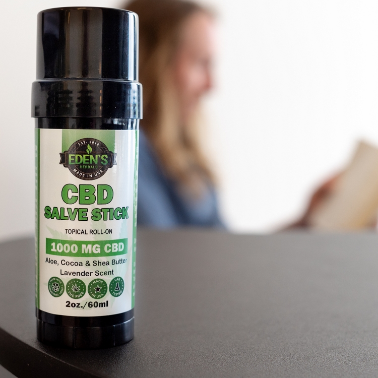 Someone reading in background with Eden's Herbals CBD salve stick in foreground