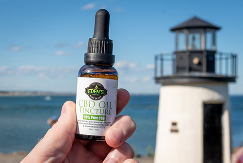 Hand holding up a CBD oil tincture from Eden's Herbals with a lighthouse in the background