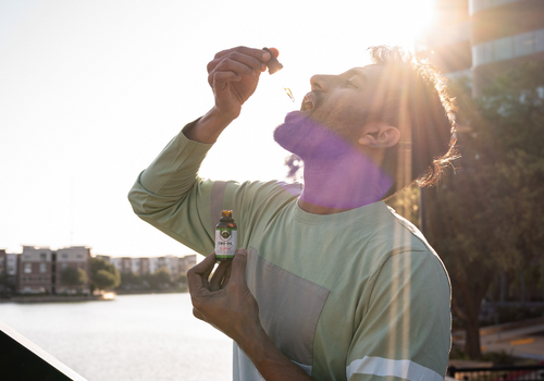 Man holding cbd oil tincture dropper to mouth with sun rising behind him