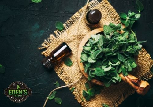 herbs in a bowl next to essential oil bottles