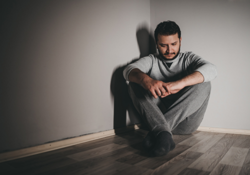 Depressed man sitting in dark corner of bedroom