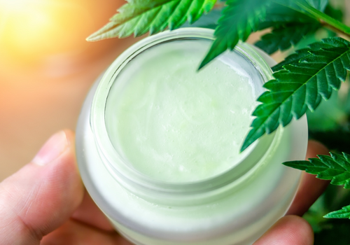 Closeup of the top of open cbd lotion jar with cannabis leaf over it