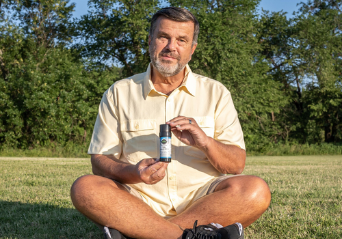 Older man sitting cross legged in field holding cbd salve stick from edens herbals