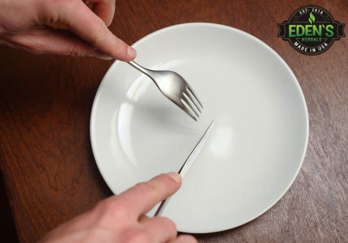 Person holding fork and knife over an empty plate