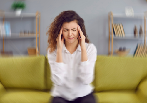 Woman sitting on couch holding head in pain from tinnitus