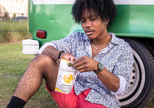 Young man sitting against a bus opening a bag of cbd gummies from eden's herbals
