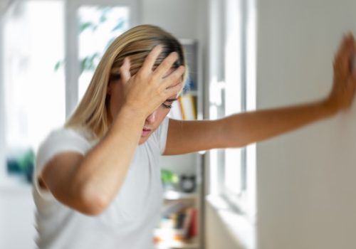 Woman leaning against door frame while clutching head in pain due to tinnitus