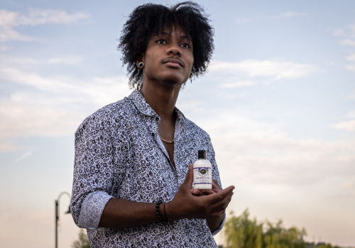 Young man holding cbd lotion bottle with sunlit sky behind him