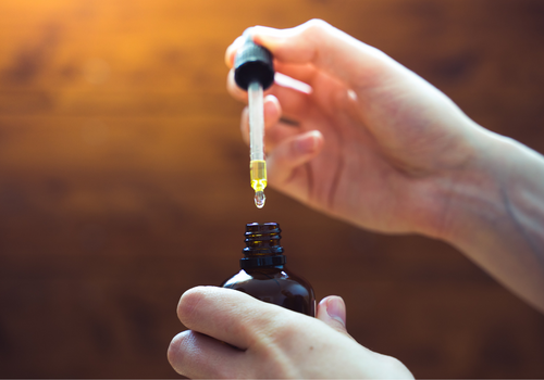 Closeup of hand holding open cbd tincture with dropper