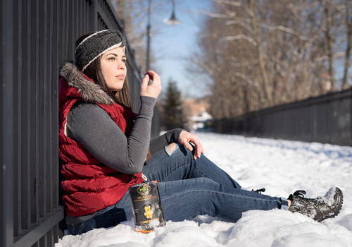 Woman sitting on a snowy bridge eating from a bag of CBD gummies