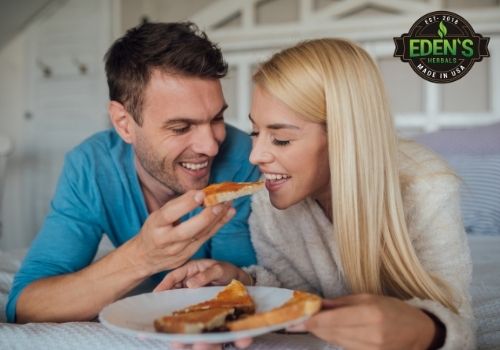 Couple laying in bed eating pizza