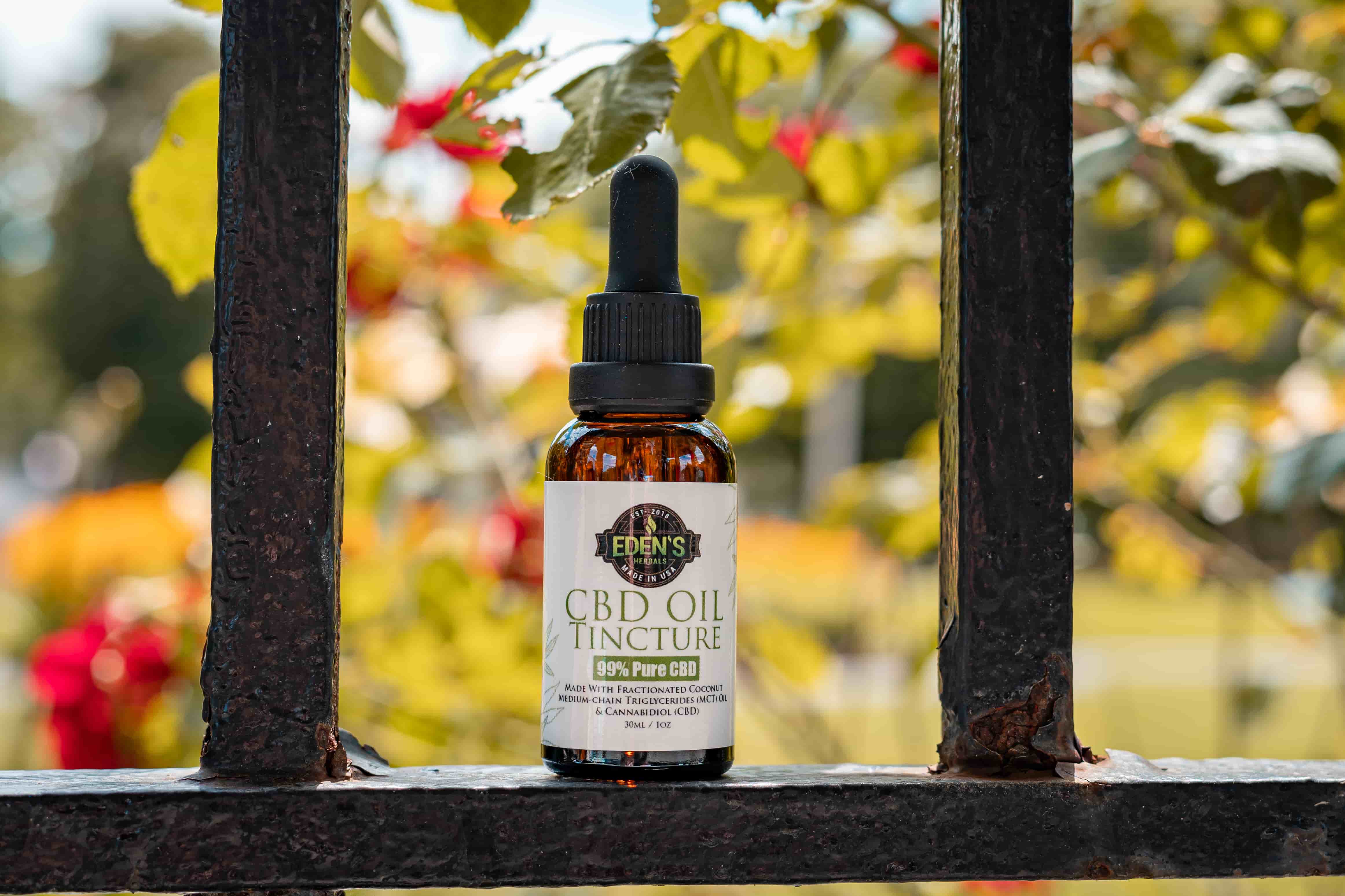 Eden's Herbals CBD Oil Tincture sitting on metal railing with flowers in background
