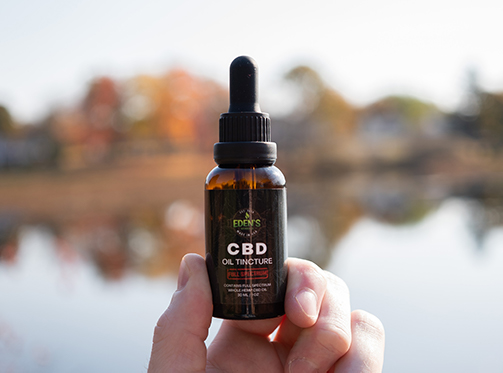 Tincture of full spectrum unflavored CBD oil from Eden's Herbals being held up in front of lake