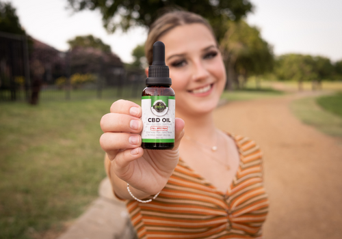 Smiling young woman on dirt path holding up bottle of full spectrum cbd oil