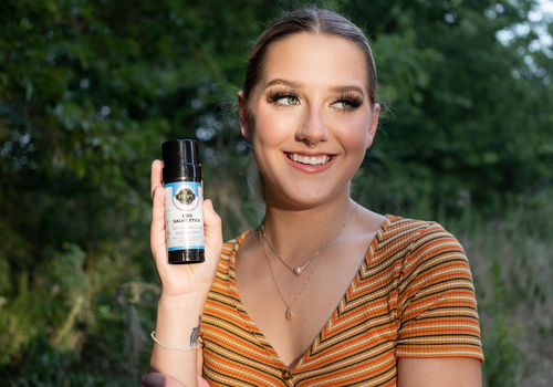 Young woman smiling and holding up a cbd salve stick from Edens Herbals