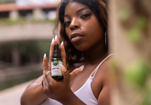 Middle age black woman holding up cbd oil tincture and looking towards camera