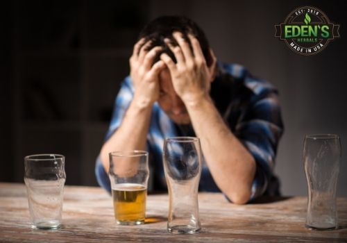 man holding head surrounded by empty glasses of beer