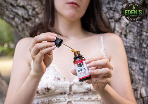 woman holding eden's herbals full spectrum CBD Oil in the woods