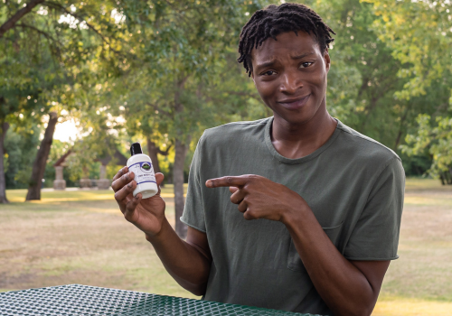 Young man holding and pointing to a bottle of cbd lotion 