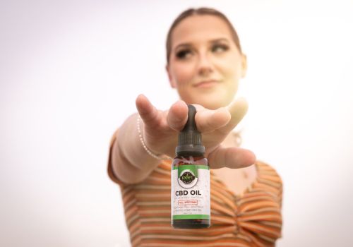 Young woman holding full spectrum cbd tincture between fingertips with sun behind her