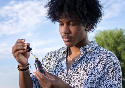 Young man holding open tincture of full spectrum cbd oil and looking at it thoughtfully